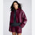 A model wearing a cropped, glossy burgundy faux-leather button-up shirt jacket, matching shorts, and a dark gray knit sweater, photographed against a light gray studio background.