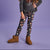 A child model wearing dark gray leggings with a brown and cream polka dot pattern, styled with a dark gray ruffled long-sleeve top and brown suede boots against a solid lavender studio background.