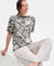 Woman wearing a patterned top and white pants sitting on a white surface.