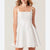 A woman wearing a white textured spaghetti-strap mini dress with a square neckline and a flared skirt, shown against a plain light beige background.