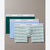 Three pairs of Calvin Klein men's boxer briefs arranged in a fan layout on a neutral taupe background. The front pair features a white base with thin green horizontal stripes, the middle pair is light blue, and the back pair is solid dark green.
