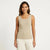 A woman modeling a ribbed knit sleeveless scoop-neck tank top in a light beige color, paired with white pants, against a plain white studio background.