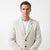 A man wearing a light beige textured blazer with small dark speckles over a white crewneck t-shirt, photographed against a clean white studio background.
