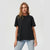 A woman modeling an oversized black short-sleeve crewneck t-shirt paired with light-wash blue jeans, set against a plain light gray studio background.