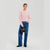 A woman modeling a light pink ribbed knit sweater, blue wide-leg jeans, and a small black handbag against a light gray studio background.