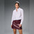 A woman modeling a white long-sleeve button-up shirt paired with a dark burgundy faux-leather mini skirt, set against a neutral gray studio background.