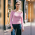 A woman wearing a light pink off-the-shoulder knit sweater and dark blue jeans, standing on a city sidewalk in front of storefront windows.