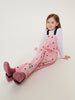 Young girl wearing pink polka dot overalls sitting on a white background