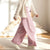 A young girl wearing a cream ribbed cardigan over a white top and pink wide-leg pants, standing in a brightly lit room with sunbeams on the wall.