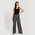 A woman modeling a pair of high-waisted, wide-leg gray trousers with a thin black belt, paired with a black tank top, against a light gray studio background.