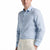 A man wearing a light blue long-sleeve linen button-down shirt and cream trousers, shown from the chest up against a plain white background.