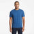 A man wearing a solid medium blue crew-neck t-shirt and dark blue jeans, standing against a clean white studio background.