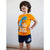 A young boy modeling a matching Jurassic World pajama set, featuring a bright orange t-shirt with a blue T-Rex graphic and 'Sleepy Saurus' text, paired with navy blue shorts.