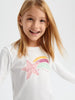 Young girl wearing a white long-sleeve shirt with colorful star design on a plain background