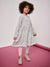 Young girl wearing a light blue dress with colorful polka dots on a pink and white background