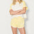 A model wearing a two-piece lounge set consisting of a short-sleeve raglan t-shirt and matching shorts in pale yellow and cream, with 'PORTORINO 03' printed on the leg.