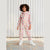 A young child wearing a hooded one-piece jumpsuit with a colorful retro bubble print, standing on a tiled floor in front of a white corrugated metal wall.