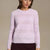 A woman wearing a light pink knit sweater with horizontal lace-like pattern bands, paired with a dark brown skirt, against a solid beige background.