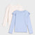 Two long-sleeve girls' knit tops on a light gray background. The front top is light blue with ruffled shoulders and scalloped hem.