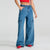 A model wearing high-waisted, wide-leg blue denim cargo pants with large patch pockets on the thighs, styled with a red crop top and red shoes against a light gray studio background.