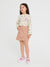 Young girl wearing a patterned top and beige skirt on a white background