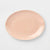 A minimalist, oval-shaped ceramic serving platter in a soft peach-pink color, shown from a top-down perspective on a clean white background.