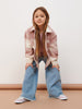 Young girl wearing a plaid shirt and jeans on a plain background