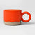 A ceramic mug with a vibrant orange glossy glaze and a textured, unglazed sandy beige base, featuring a matching circular handle.