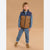 A young boy modeling a two-tone brown and navy quilted puffer vest over a blue long-sleeve shirt and matching blue sweatpants, standing against a solid tan studio background.