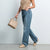 A model wearing high-waisted, wide-leg blue jeans, a beige sleeveless top, and beige loafers, holding a beige handbag against a light gray studio background.