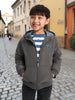 Child wearing a gray jacket with a logo on a cobblestone street
