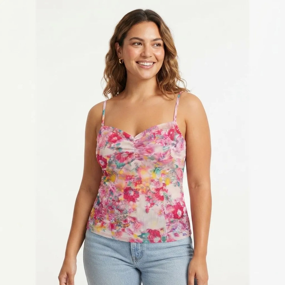 A woman modeling a floral spaghetti-strap camisole top with a sweetheart neckline, paired with light-wash jeans, against a plain white studio background.