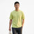 A man wearing a light lime green ribbed short-sleeve t-shirt and dark gray pants, holding a white tote bag against a plain white background.