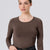 A woman modeling a long-sleeve crewneck top in a solid dark brown color, paired with black jeans and a black belt, against a solid light gray background.