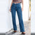 A person wearing high-waisted, wide-leg blue denim jeans with a brown cropped top and brown sandals, standing outdoors against a white wall on a stone path.
