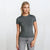 A woman modeling a fitted short-sleeve crewneck t-shirt in dark gray, paired with light gray jeans, against a plain white studio background.