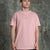 A man wearing a light pink crewneck t-shirt with a small 'UPPY TRUCK' logo on the chest, standing against a textured gray concrete wall.