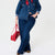A model wearing a dark blue denim jacket and matching flare jeans, styled with a red neck scarf, leopard print shoes, and carrying a red handbag against a plain white background.