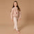 A young girl stands barefoot against a solid beige studio background, wearing a fuzzy light pink long-sleeve sweater with a reindeer face graphic and light beige pants.