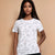 A woman modeling a white short-sleeve crewneck t-shirt with a black line art print of various animals, paired with black pants, against a solid beige background.