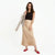 A woman modeling a beige satin midi skirt paired with a black sleeveless top, a light gray blazer draped over her arm, and red flats, set against a plain white studio background.