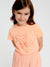 Young girl wearing a peach-colored t-shirt with a starfish design on a plain background