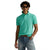 A man wearing a short-sleeve polo shirt in a vibrant mint green color, styled with blue jeans, a brown leather belt, sunglasses, and a wristwatch, set against a plain white background.