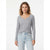 A woman modeling a light gray ribbed long-sleeve henley top with a split V-neck, paired with light-wash blue jeans, against a plain white studio background.