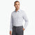 A man wearing a light gray and white micro-check patterned long-sleeve dress shirt with dark gray trousers, standing against a plain white studio background.