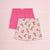 Two pairs of children's boxer shorts laid flat on a pale pink background. The back pair is solid bright pink, and the front pair is light pink with an allover print of playful brown cats.