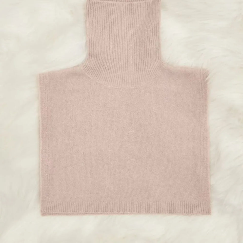 A pale blush pink ribbed knit turtleneck sweater laid flat on a white faux fur background.