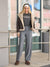 Woman wearing a black t-shirt with text, gray pants, and a beige jacket standing in front of a glass building.
