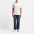 A man wearing a plain white short-sleeve crewneck t-shirt, blue jeans, and white sneakers, standing against a clean white studio background.
