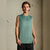 A man wearing a sage green sleeveless athletic tank top with a small black logo on the chest, standing against a textured concrete wall.